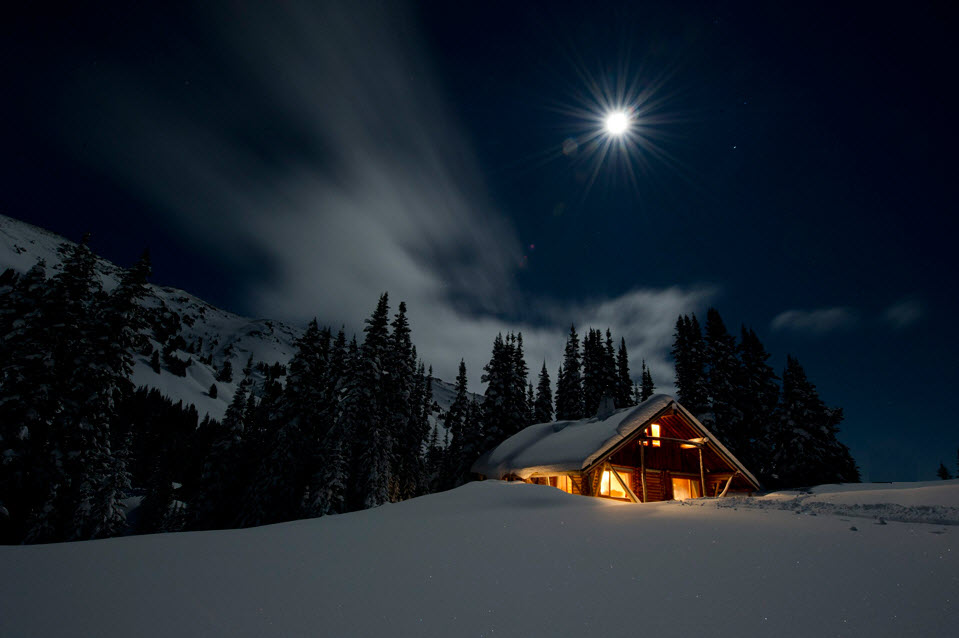 Houten blokhut in een besneeuwd berglandschap bij nacht